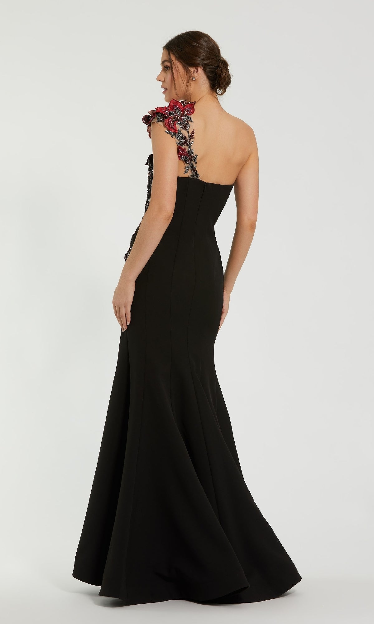Model showcases the Mac Duggal 11779: a one-shoulder black formal dress with a floor-length mermaid skirt and bold red floral appliqué on the shoulder, viewed from the back.